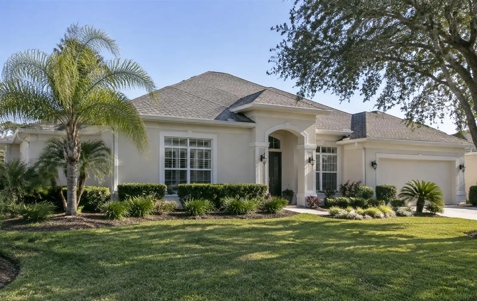 Elegant Central Florida stucco home with white gutters and downspouts under live oaks at sunset
