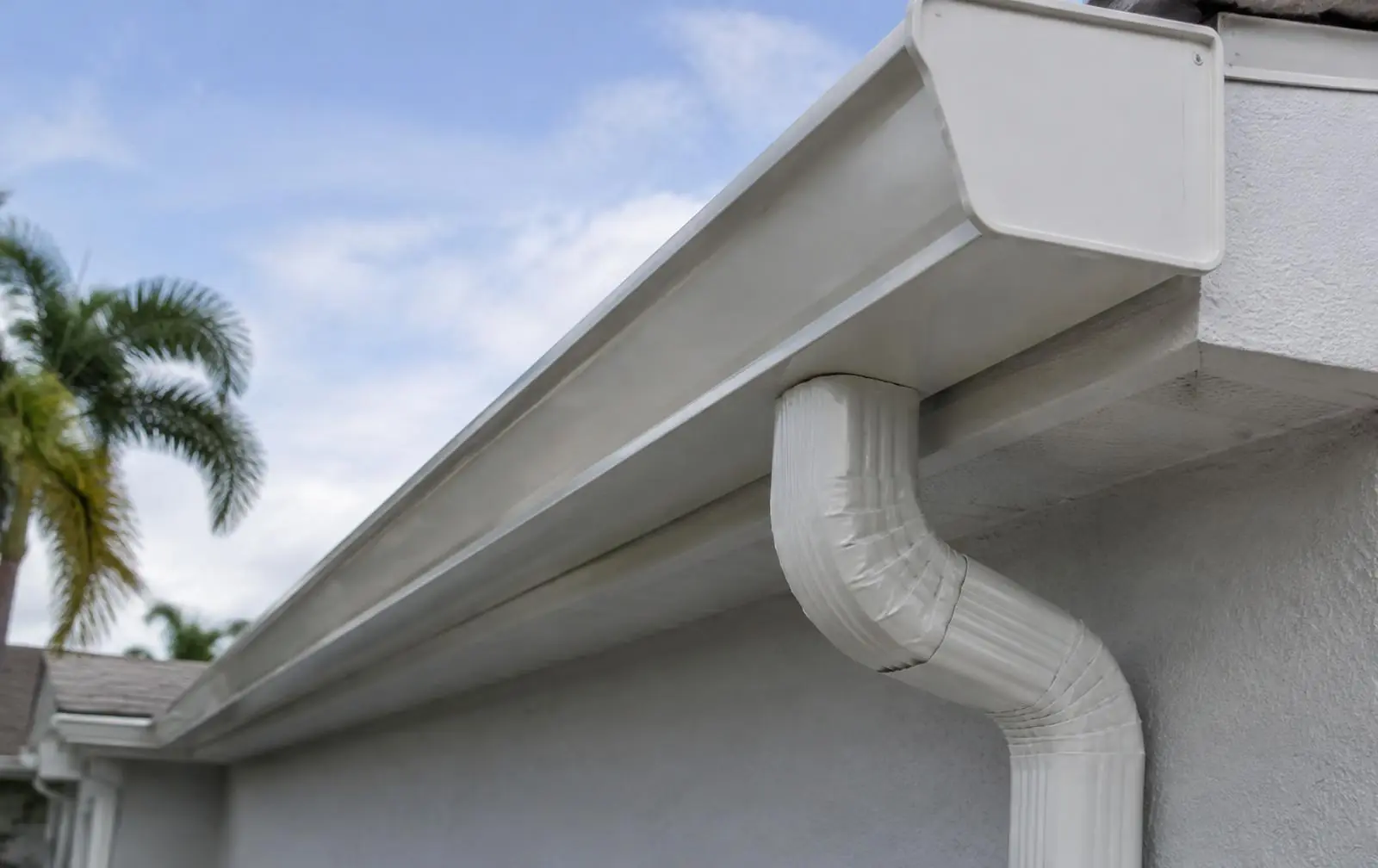 White seamless gutter with end cap and downspout outlet on a gray stucco Florida home